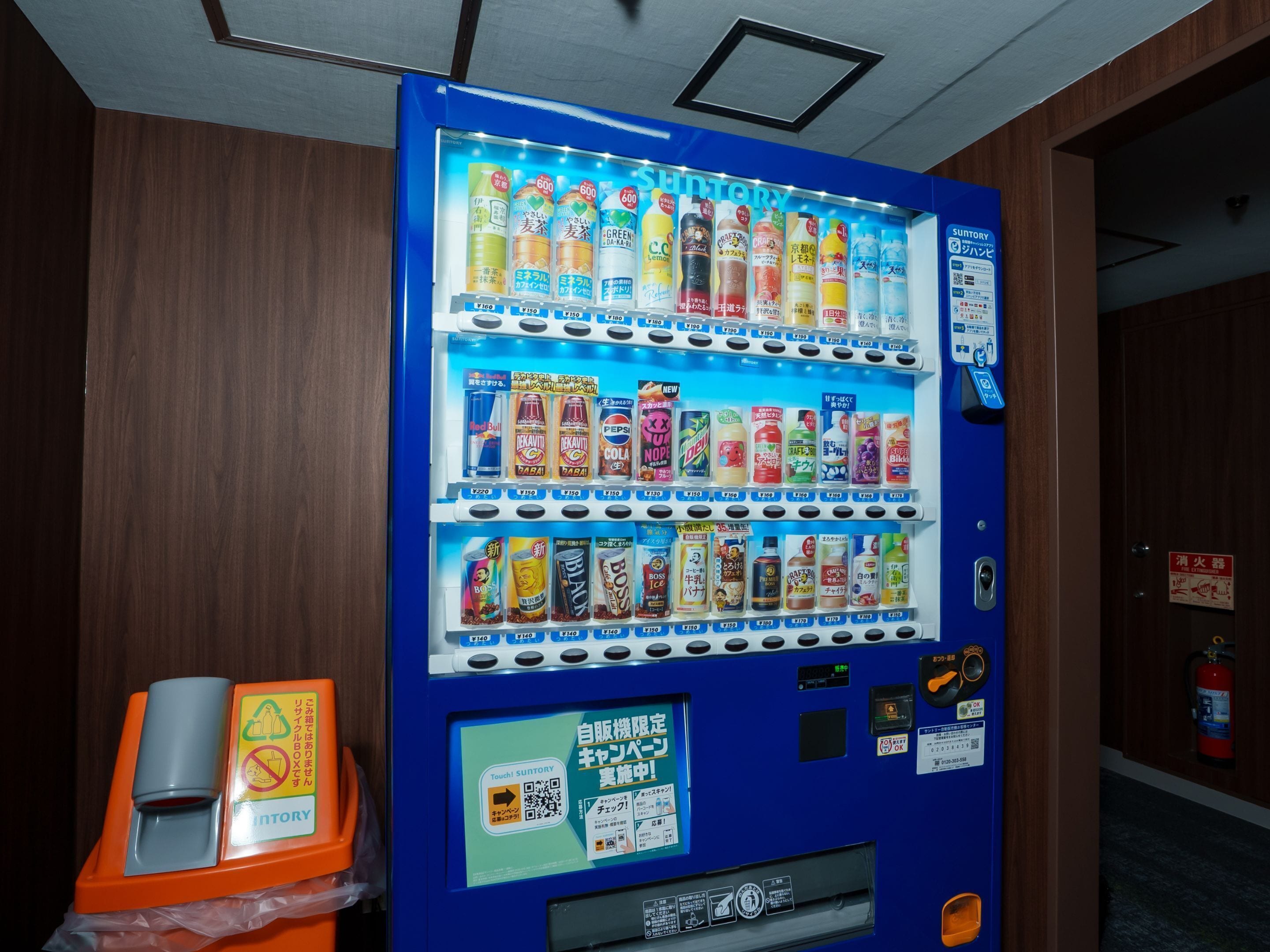 Máquina de vendas com diversas opções de bebidas e uma lixeira.
