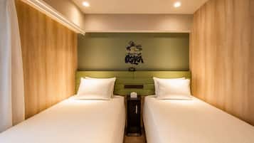 A hotel room with two single beds, a green headboard, a wall-mounted coat rack, and a ceiling light.