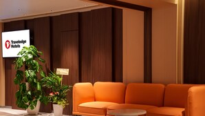 Um hall moderno com painel de madeira, um letreiro da Travelodge Hotels, uma grande planta em vaso, um sofá laranja e uma mesa de centro redonda.