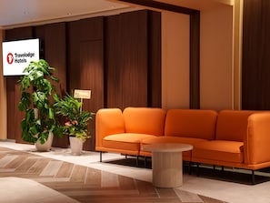 A modern lobby with a wooden panel wall, a Travelodge Hotels sign, a large potted plant, an orange sofa, and a round coffee table. - Travelodge Osaka Shinsaibashi (Osaka)