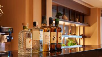 Uma área de bar com várias garrafas de bebidas alcoólicas, incluindo uísque e saquê, sobre uma superfície refletora.