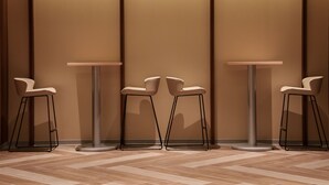 Um interior moderno com três mesas redondas e cadeiras combinando, cada uma com base de metal, posicionadas diante de uma parede com painéis verticais.