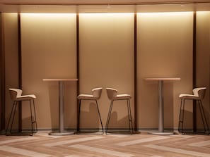 A modern interior with three round tables and matching chairs, each with a metal base, positioned against a wall with vertical panels. - Travelodge Osaka Shinsaibashi (Osaka)