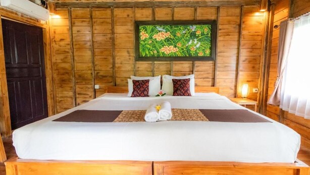Una habitación de madera con una cama, un cuadro floral enmarcado en la pared y una puerta oscura.