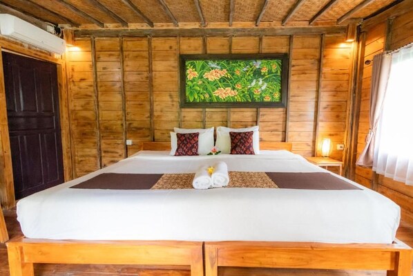 A wooden room with a bed, a framed floral artwork on the wall, and a dark door.