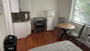 Une cuisine compacte avec des meubles blancs, un plan de travail en granit, un micro-ondes encastré, un petit réfrigérateur et un coin repas avec une table ronde et des chaises.