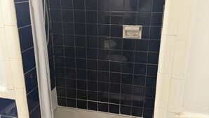 Une salle de bain avec des murs recouverts de carreaux bleu foncé, un rideau de douche blanc et un lavabo blanc.