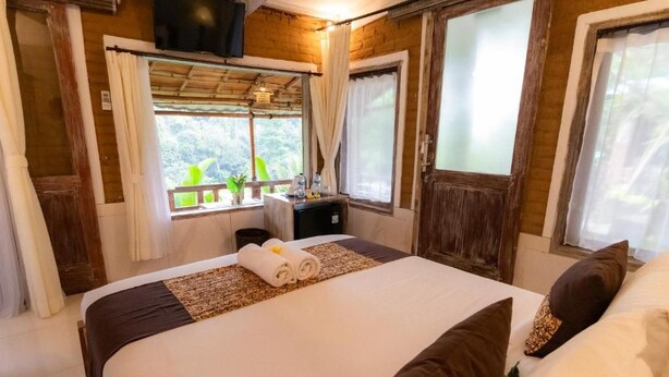 A bedroom with a large bed, a small desk, and a window with curtains. - Room-romantic Jungle Nest (Ubud)