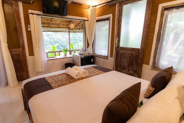 A bedroom with a large bed, a small desk, and a window with curtains. - Room-romantic Jungle Nest (Ubud)