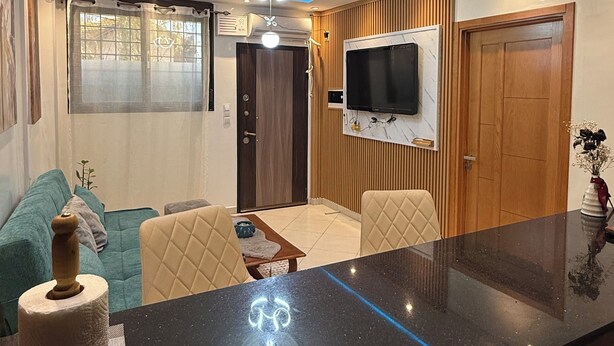 Uma sala de estar moderna com bancada de mármore preto, luminária no teto, televisão na parede e porta de madeira.