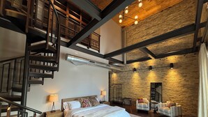 Een ruime slaapkamer met een groot bed, een houten trap en een stenen muur.
