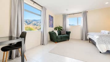 Una habitación moderna con cama, sofá verde, escritorio con silla y ventanas grandes con cortinas.