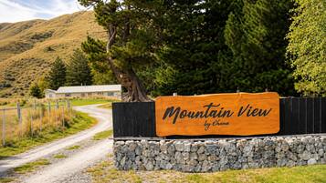 A wooden sign with 'Mountain View by Chana' written on it, a gravel path, a fenced area, and a building in the background.