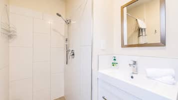 Een badkamer met een douche, een wastafel met spiegel en een handdoekrek.