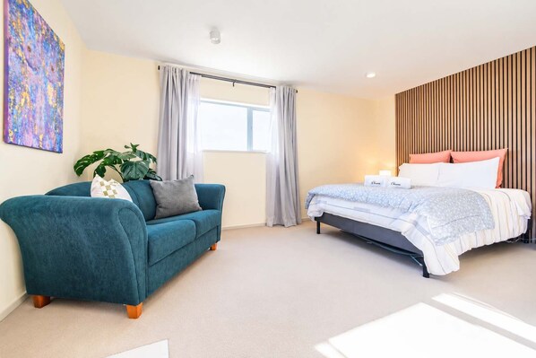 A modern bedroom with a bed, a sofa, a potted plant, and a painting on the wall.