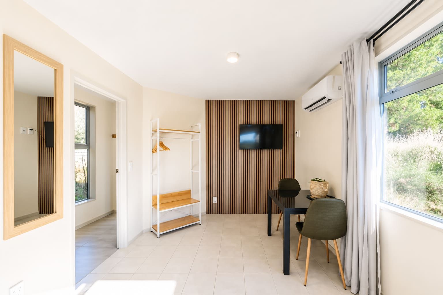 Quarto moderno com TV, painel de parede de madeira, um banco e uma mesa com cadeiras.