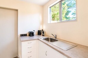 A compact kitchenette with a sink, a coffee maker, a toaster, and a window with a view of trees.