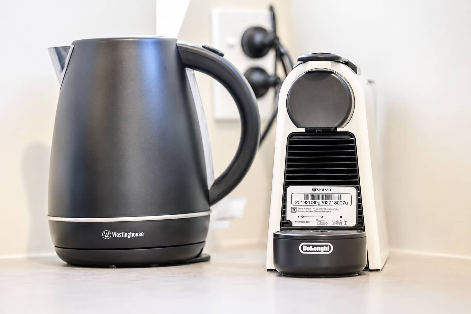 A black electric kettle and a Delonghi espresso machine on a kitchen counter.