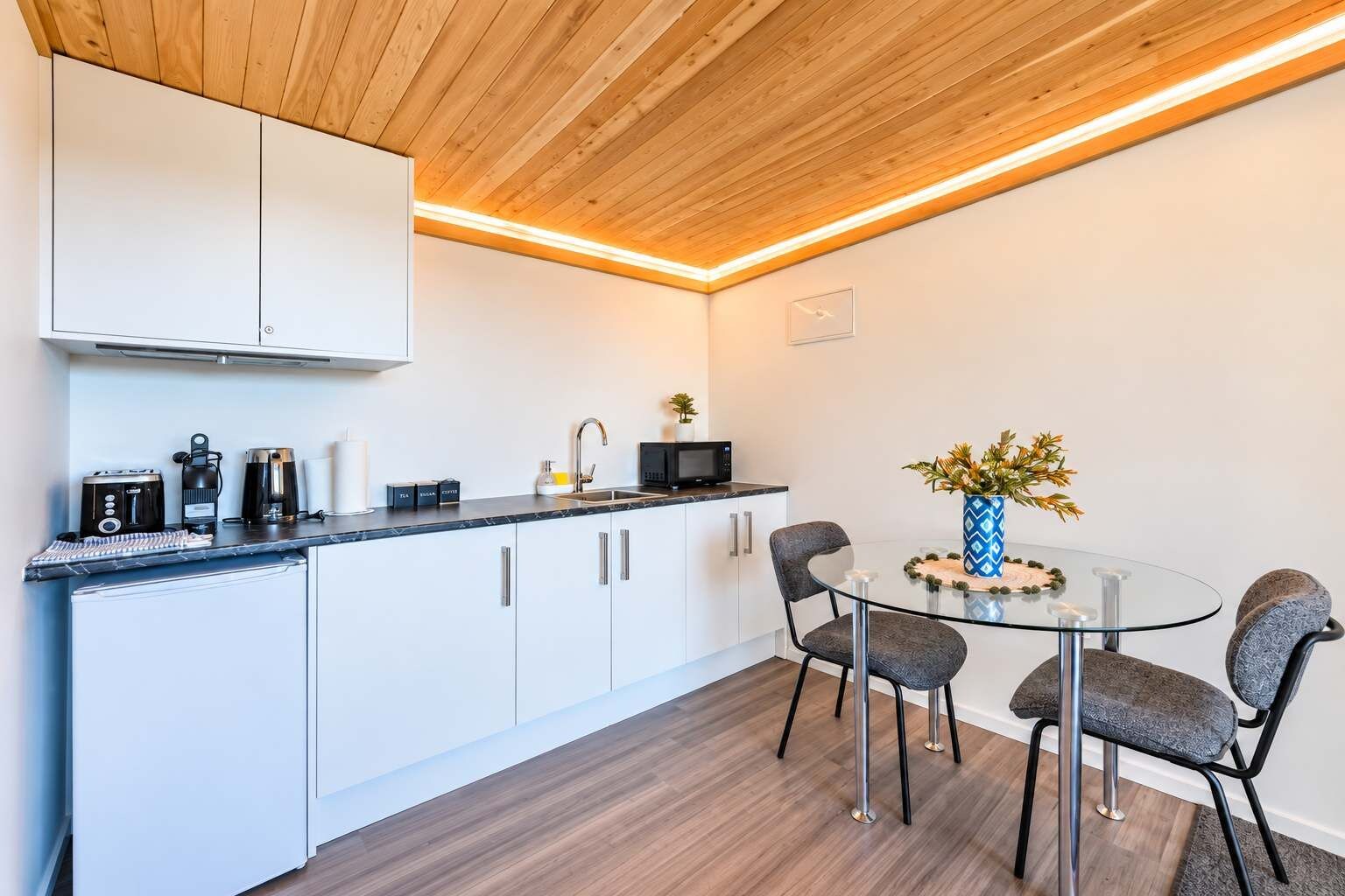 Een moderne keuken met witte kasten, een zwart aanrecht en een ronde glazen tafel met stoelen.
