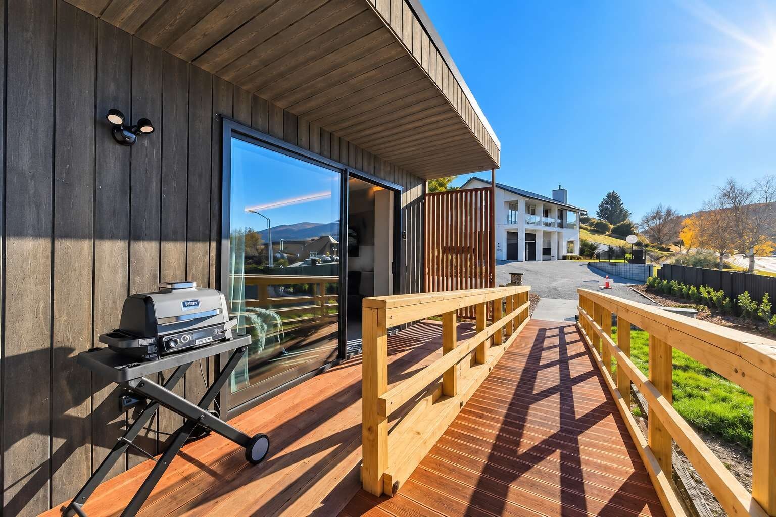 A wooden deck with a barbecue grill, a glass door leading to a building, and a clear view of a residential area.