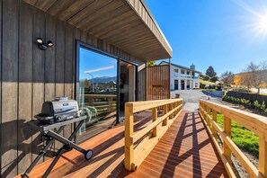 Eine Holzterrasse mit einem Grill, eine Glastür, die zu einem Gebäude führt, und freie Sicht auf eine Wohngegend.