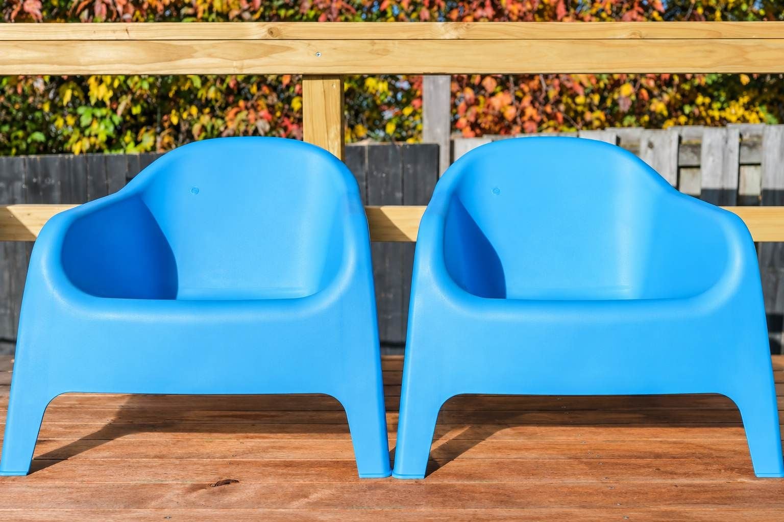 Twee blauwe plastic stoelen met een houten bankje op de achtergrond.