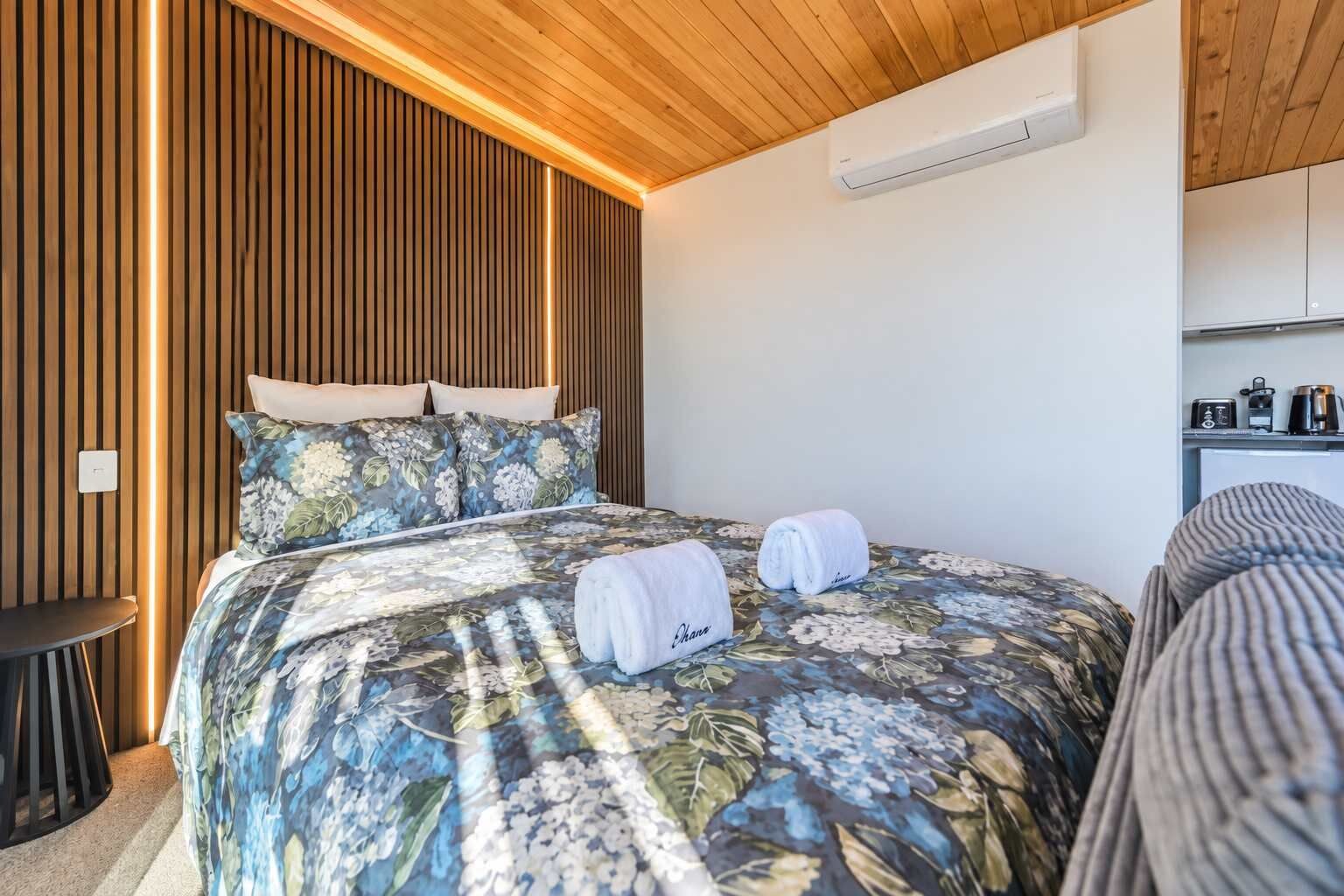 Un dormitorio con cama, almohadas, mesita de noche y aire acondicionado instalado.