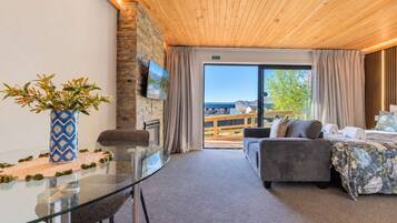A hotel room with a glass table, a sofa, a bed with floral bedding, a fireplace, and a view of the outdoors.