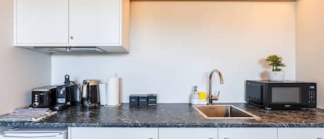 Une cuisine compacte dotée d’un plan de travail noir, de meubles blancs, d’un évier en acier inoxydable, d’un four à micro-ondes et d’un grille-pain.