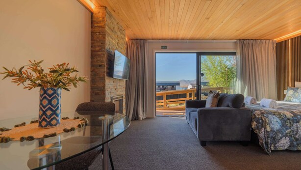 Une chambre d’hôtel moderne avec une table à manger en verre, un canapé, un lit, une télévision et une vue sur l’extérieur.
