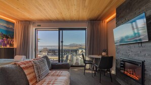 A hotel room with a bed, a TV, a fireplace, and a view of the outdoors. - Aurora Vista - Ohana (Lake Tekapo)