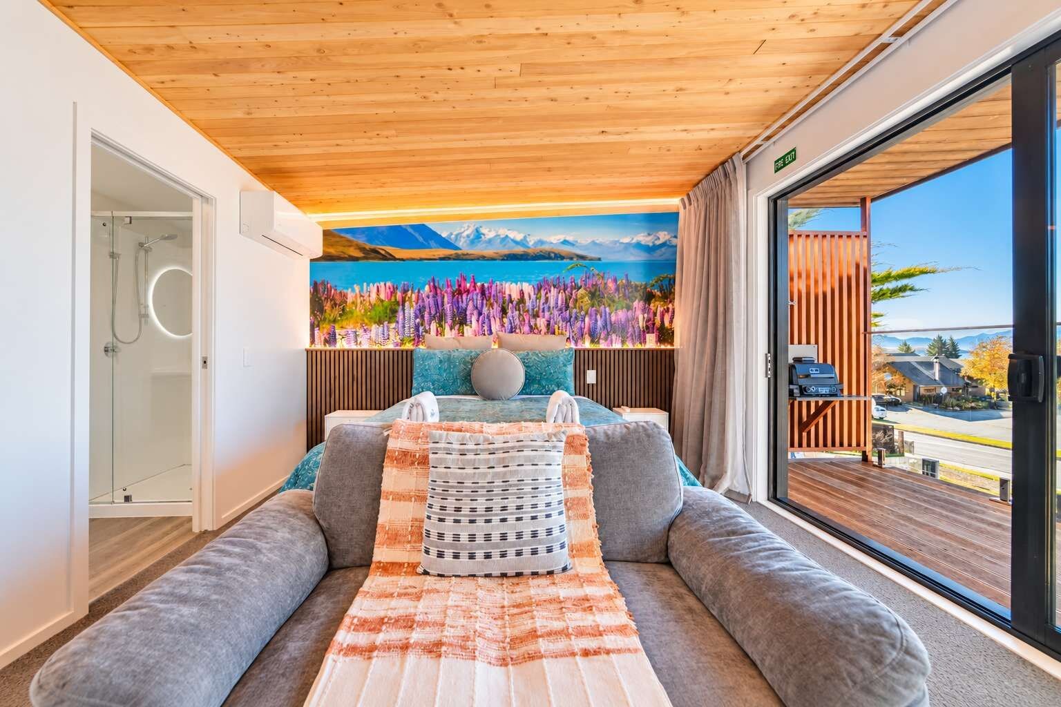 A modern bedroom with a large bed, a sofa, a view of the outdoors, and a painting on the wall.