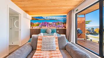 A modern bedroom with a large bed, a sofa, a view of the outdoors, and a painting on the wall.