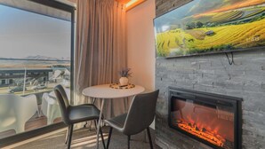 A modern room with a fireplace, a dining table with chairs, a TV mounted on the wall, and a large window with curtains. - Aurora Vista - Ohana (Lake Tekapo)
