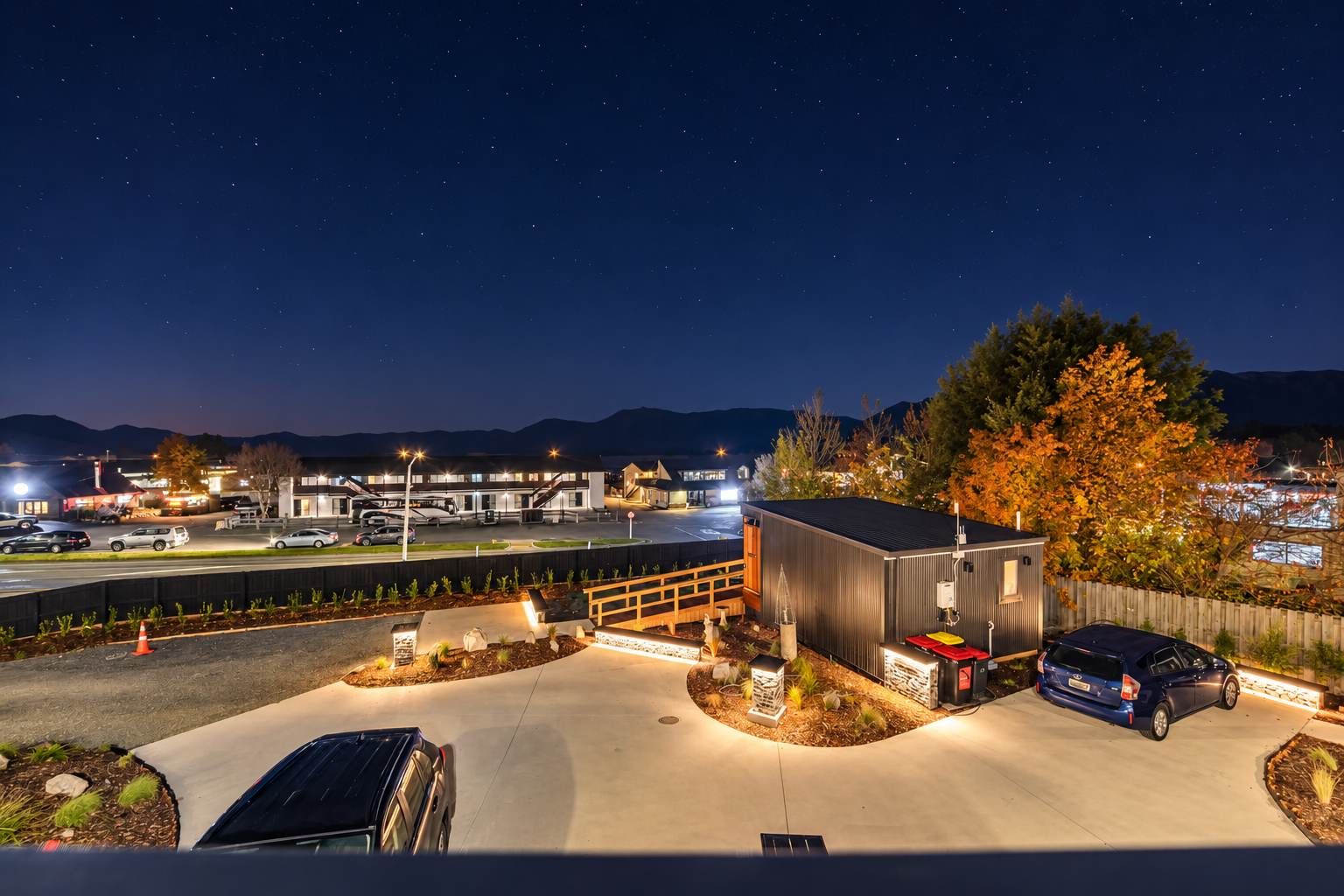 A parking area with a building, a car, and a tree.