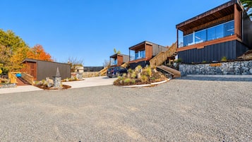 A modern building with a gravel driveway, a car, and a wooden bridge.