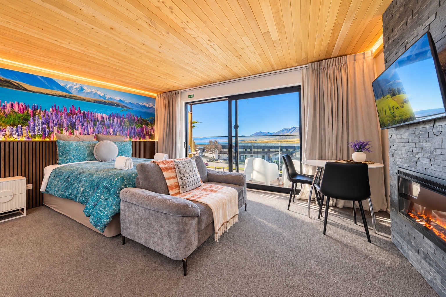 A modern hotel room with a bed, a sofa, a dining area, and a fireplace.