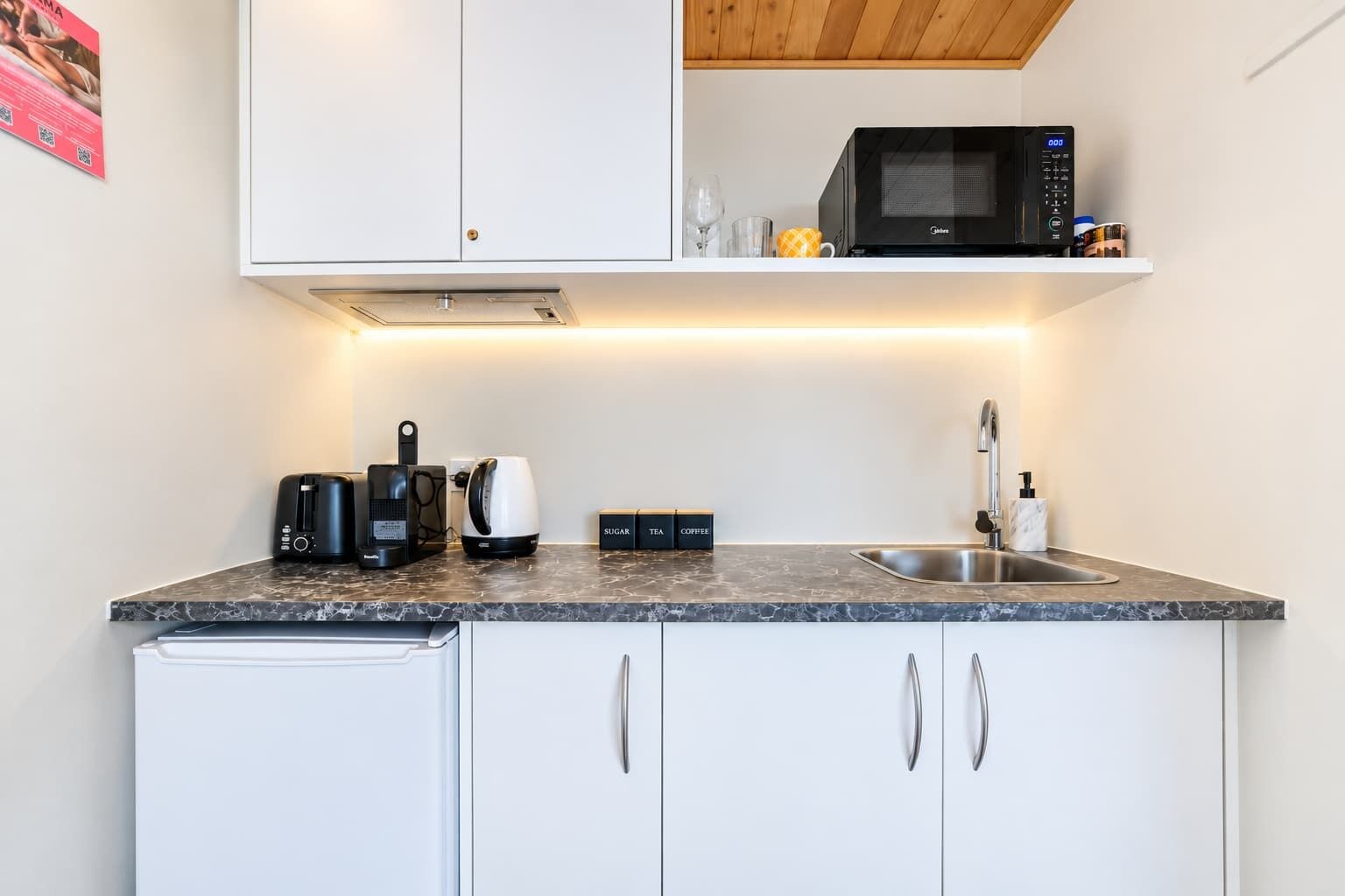 Une cuisine moderne équipée d’un four à micro-ondes, d’une machine à café et d’un appareil à préparer le thé, le tout posé sur le plan de travail.