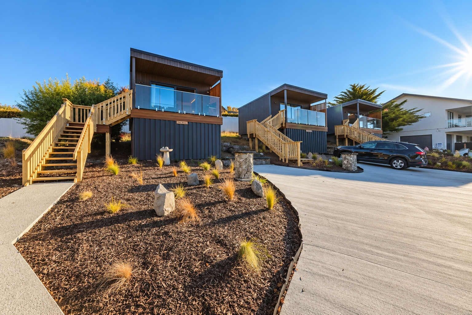A modern building with a wooden staircase, a parking area, and a landscaped garden with rocks and plants.