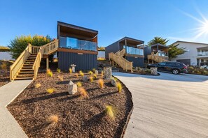 A modern building with a wooden staircase, a parking area, and a landscaped garden with rocks and plants.