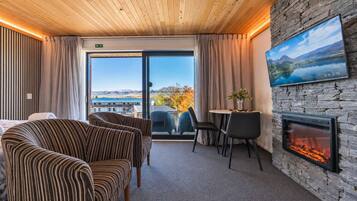 A hotel room with a fireplace, a dining area, and a large window with a view of mountains and a lake.