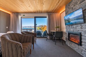 Et hotelværelse med pejs, spiseplads og stort vindue med udsigt til bjerge og sø.