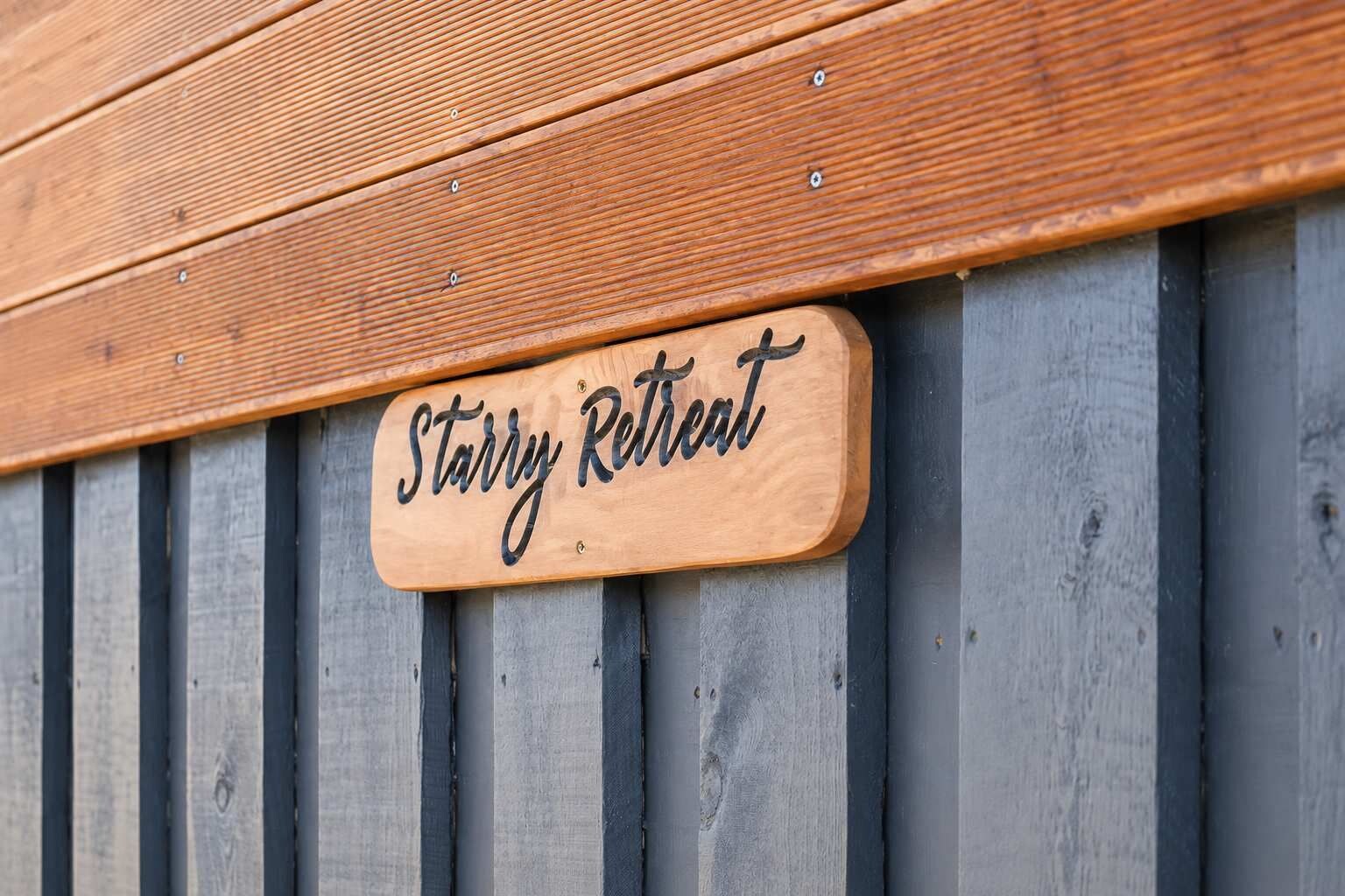 A wooden sign with the text 'Starry Retreat' mounted on a grey vertical wooden panel.
