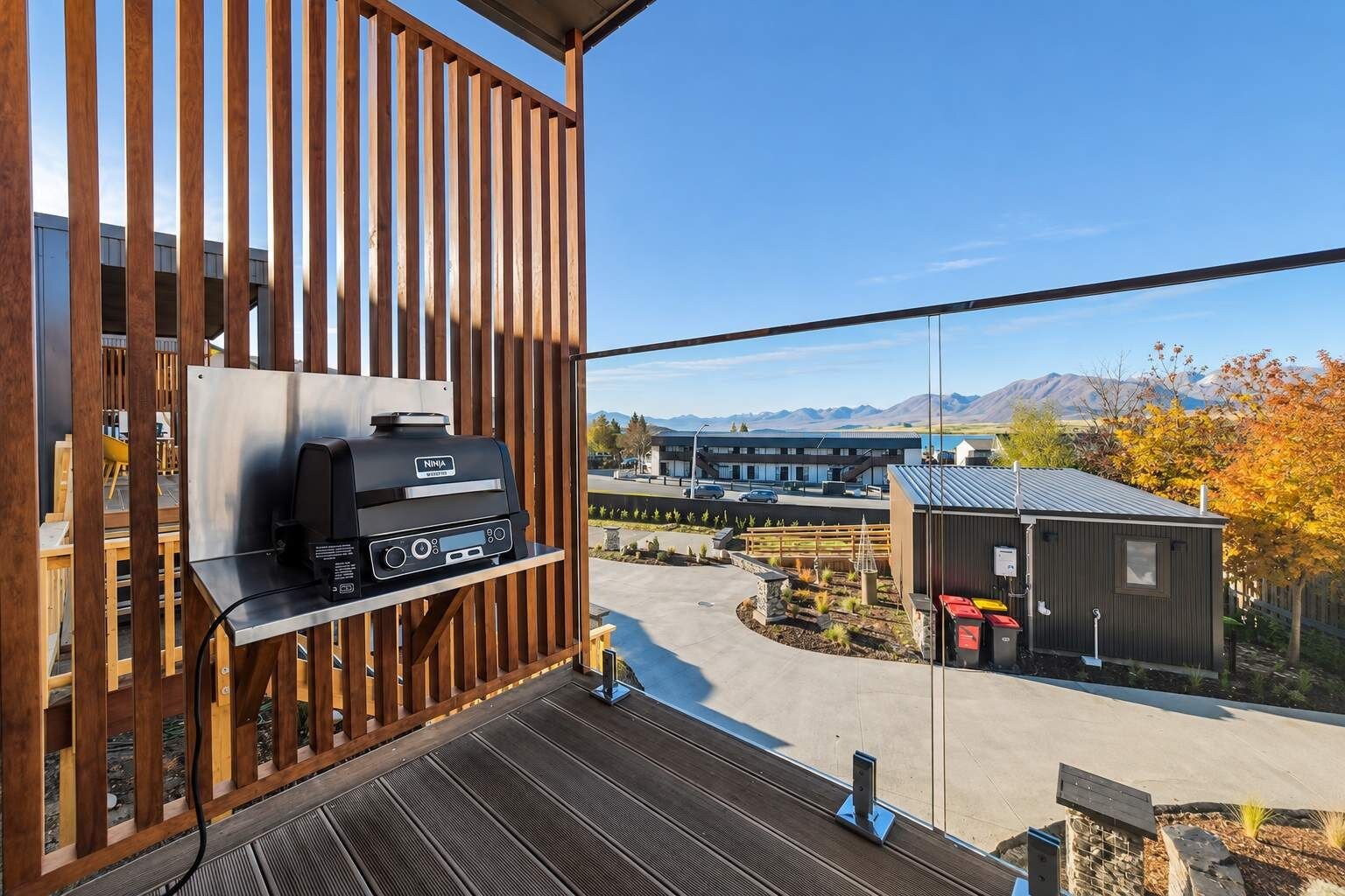 A balcony with a grill, a view of a building, and a mountainous landscape.