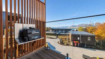 A balcony with a grill, a view of a building, and a mountainous landscape.