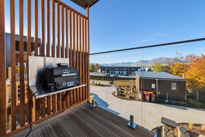 A balcony with a grill, a view of a building, and a mountainous landscape.