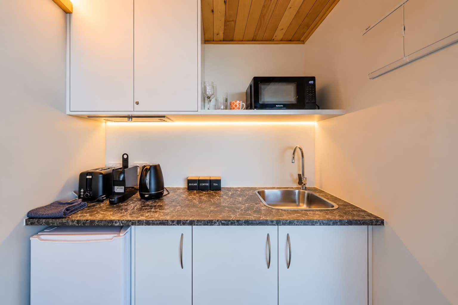A compact kitchenette with a microwave, toaster, coffee maker, and a sink.