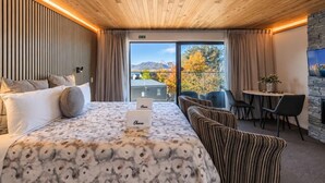 A hotel room with a large bed, a dining area, and a view of the outdoors. - Starry Retreat | Lake Views + Fireplace (Lake Tekapo)
