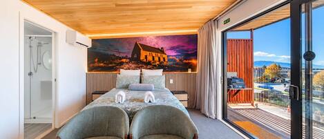 Habitación de hotel con cama, dos sillones, ducha, ventana grande con vistas y un mural en la pared.