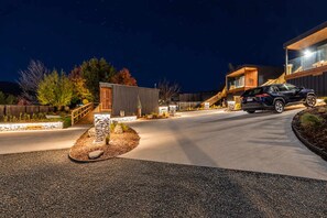 Une maison moderne avec une allée, une voiture garée dans la rue et un éclairage extérieur soigné la nuit.